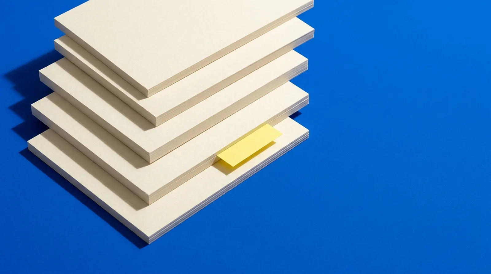 A stack of blank cream cards with a yellow tab on a cobalt background